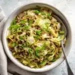 Egg roll in a bowl keto served in a white bowl with cabbage, meat, and green onions on a bright marble surface.