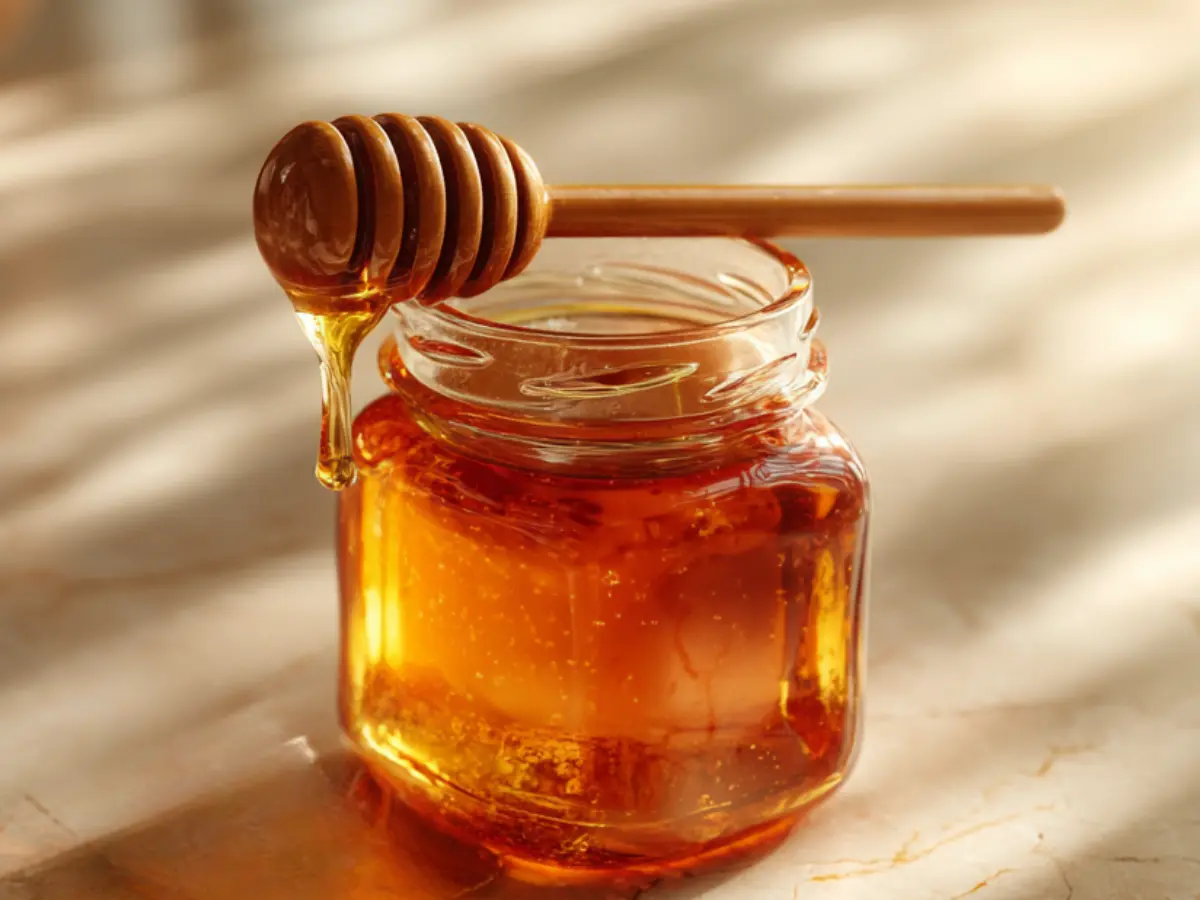 Homemade hot honey recipe in a glass jar with a wooden dipper on a marble countertop.