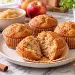 Moist applesauce muffins with cinnamon and fresh apples on a marble kitchen countertop.