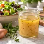 White balsamic Vinaigrette in a glass jar beside fresh salad greens on a marble countertop