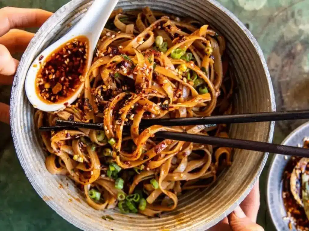 Bowl of noodles topped with homemade chili crunch, crispy garlic, and sesame seeds
