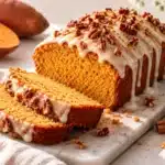 Moist sweet potato pound cake baked in a rectangular loaf pan, topped with vanilla glaze and chopped pecans.